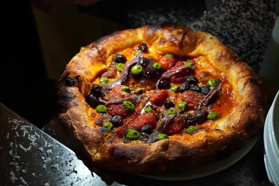 Anchovy and olive pizza with tomato and dots of herb sauce, blistered crust